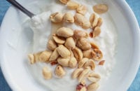 Väike valge kauss jogurtit, mille peal on maapähklid.